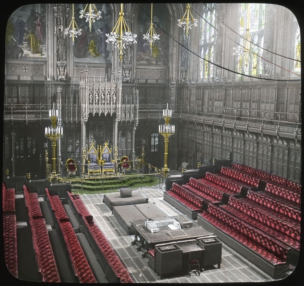 A 1913 colour lantern slide looks down into the House of Lords chamber, with a gilded throne, red facing benches, tall windows, chandeliers, wall paintings and elaborate Gothic woodwork.