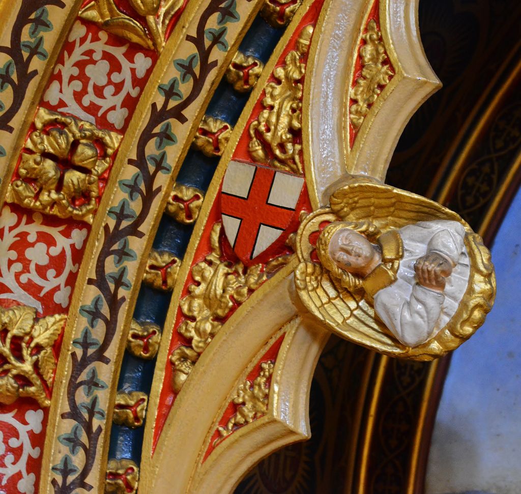 A close interior detail shows a gilded angel projecting from a cream moulded arch beside a red-and-white shield and narrow painted bands of leaves, flowers and gold ornament.