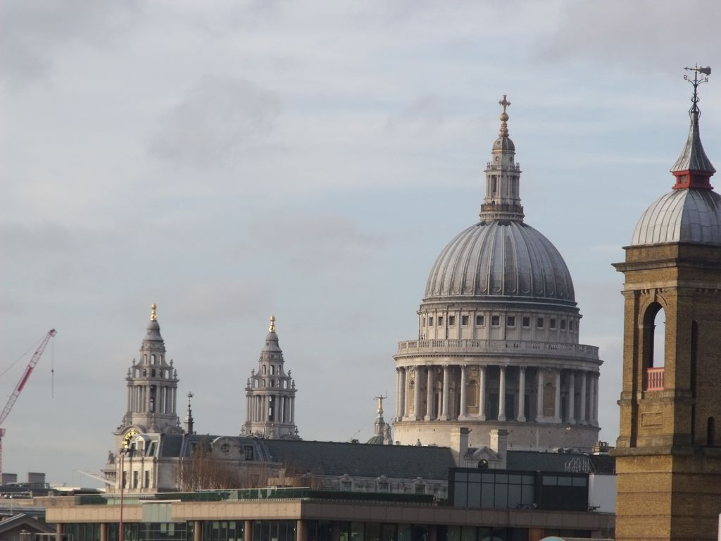 The great dome and paired western towers of St Paul's rise above modern riverside roofs, with a crane and another tower at the edges of the hazy skyline.