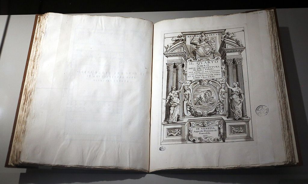 A large old book lies open under museum lighting, with a blank verso at left and an elaborate engraved Italian architectural title page dated 1570 at right.