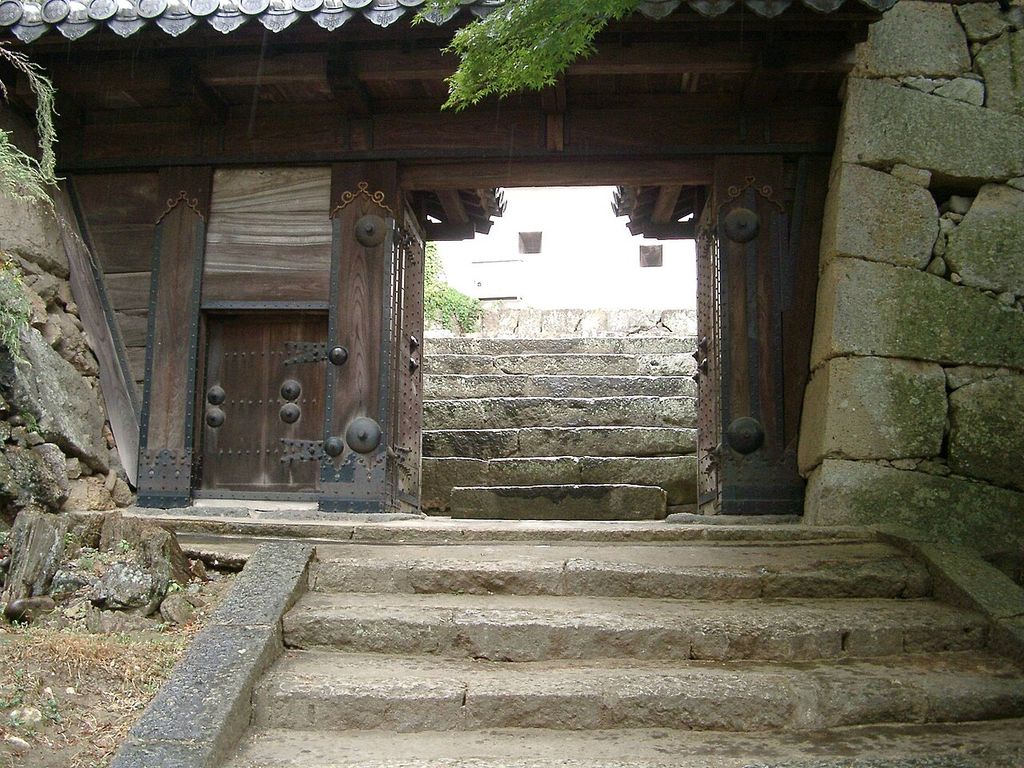A heavy timber gateway with iron fittings frames ascending stone steps between masonry walls.