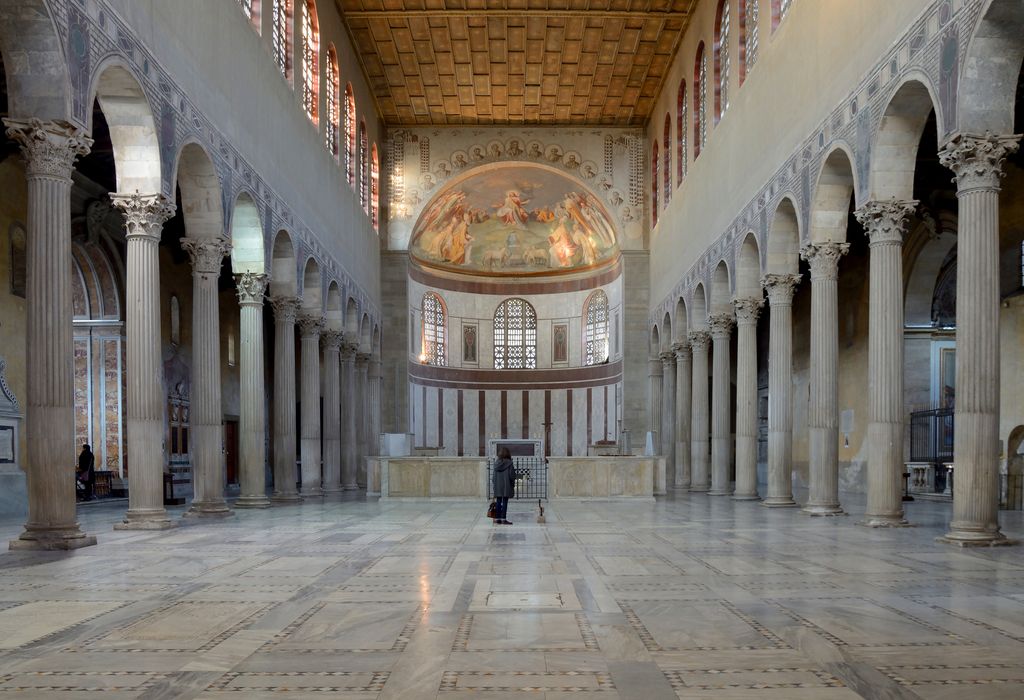 A broad marble nave runs between arcades and lower aisles toward an apse, with high windows and a timber ceiling above later furnishings.