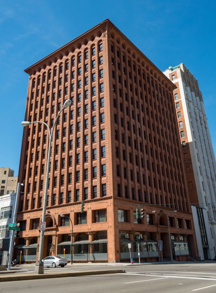 A tall reddish terracotta office building rises from an ornate arcaded base through many narrow window bays to rounded top arches and a projecting cornice.