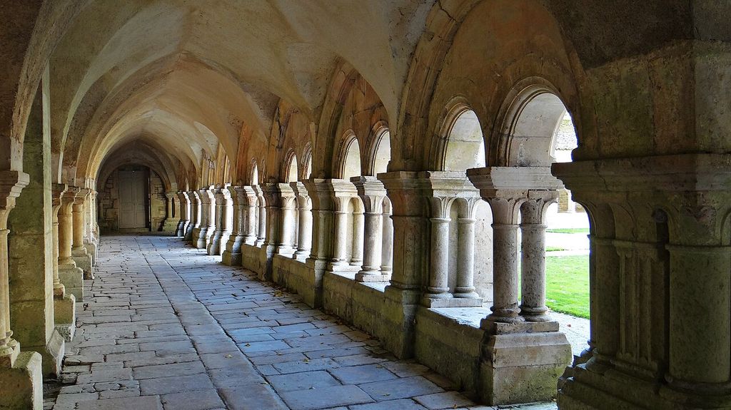 A vaulted stone cloister walk recedes beside paired columns and round arches, opening onto a bright green court.