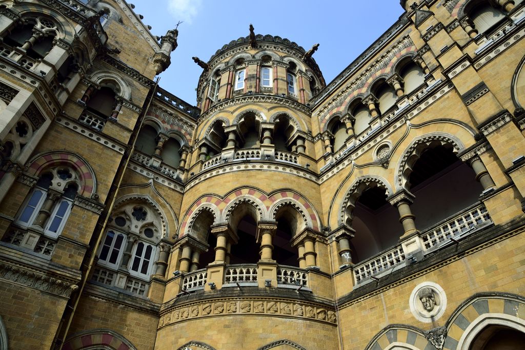 A low-angle view fills the frame with layered arcades, balconies, carved bands, coloured stone columns and part of a domed central mass.