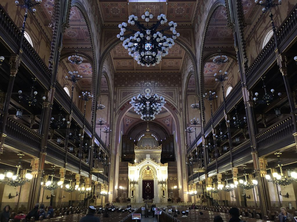 Two dark gallery tiers flank a tall richly patterned sanctuary filled with arches, chandeliers, decorated ceiling panels and rows of seats.