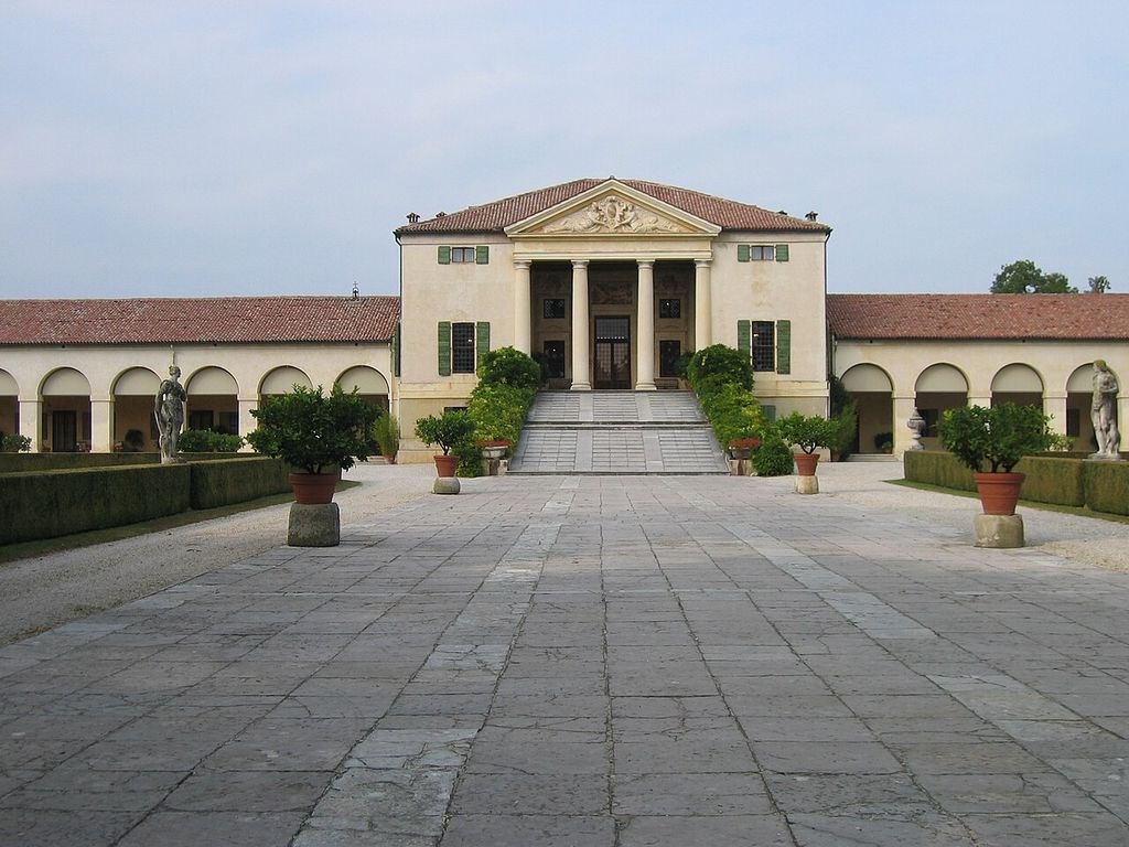 A temple-fronted villa reached by a broad ramp is joined to long single-storey arcades extending across both sides of the image.