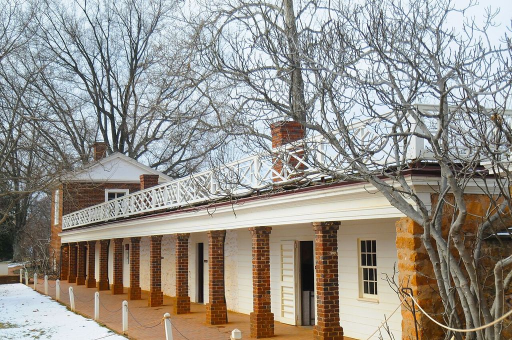 Brick piers, doors and windows line a covered service passage beneath a white balustraded terrace, with snow and leafless trees nearby.