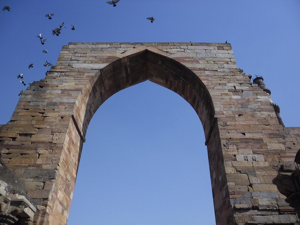 A tall pointed opening pierces a stone screen with predominantly horizontal masonry courses.