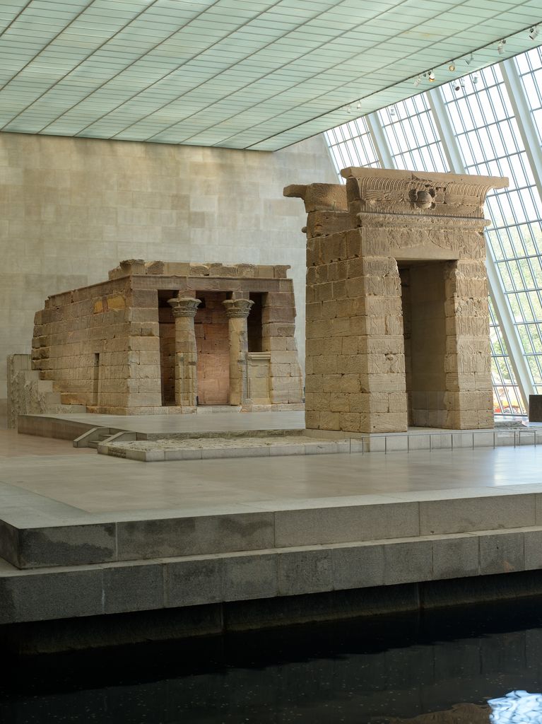 Two carved stone columns support a small temple porch beneath the museum’s glazed roof.