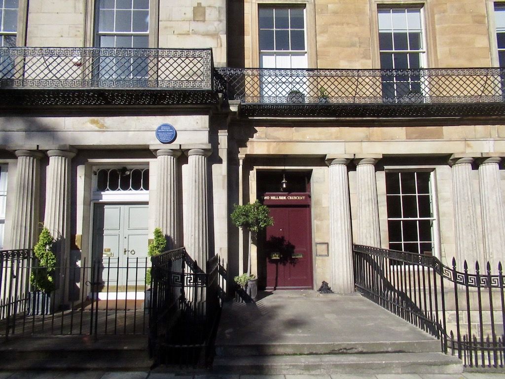 Paired fluted columns frame townhouse entrances below iron balconies edged with a Greek-key pattern.