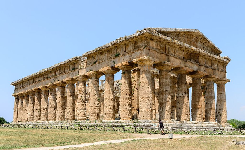 A long sandstone temple has closely spaced fluted columns supporting a weathered entablature and triangular pediment.