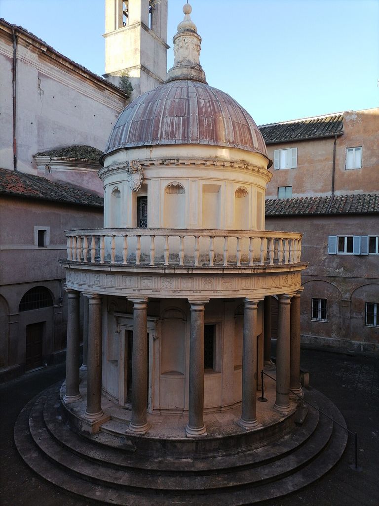 A circular colonnade and continuous carved entablature wrap a small domed memorial inside a close-walled courtyard.