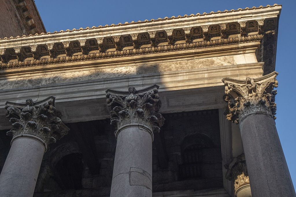 Three leafy Corinthian capitals top grey granite shafts beneath a deep stone entablature with brackets and carved mouldings.