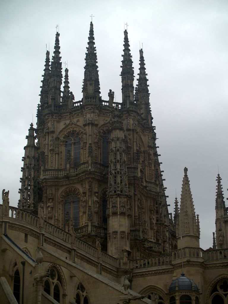A tall octagonal stone lantern rises behind open parapets, with traceried windows, pinnacles, statues and dense carved ornament under an overcast sky.