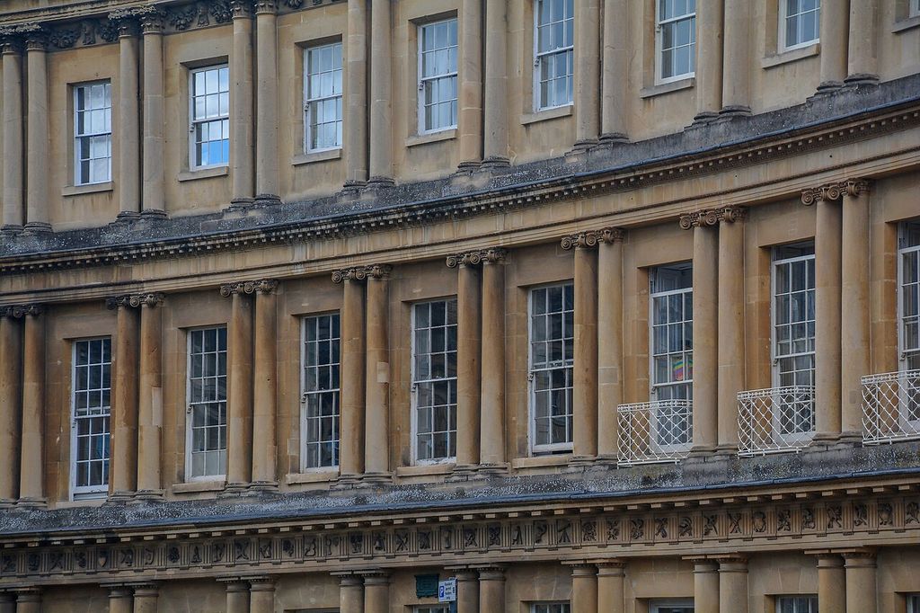 Columns and horizontal entablatures divide a curved stone façade into storeys and repeated window bays.