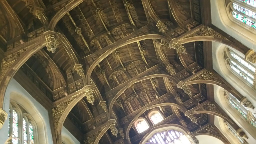 Carved timber members and arched braces repeat across a high hall beside bright upper windows.