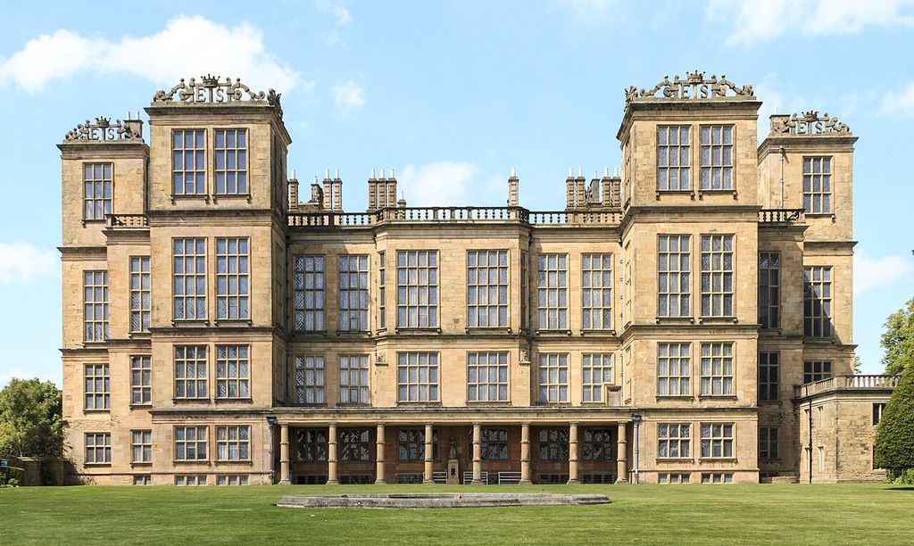 Repeated mullioned windows divide the stone façade and its projecting towers into tall bays.
