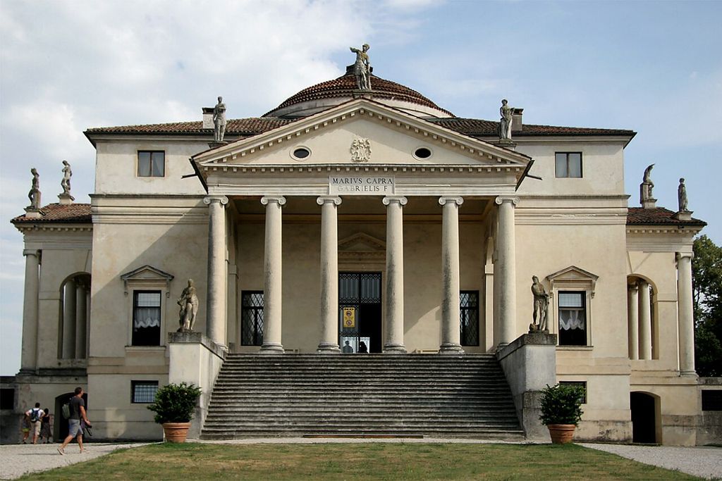 A broad stair rises to six columns and a triangular pediment on a symmetrical pale villa, with a dome behind.