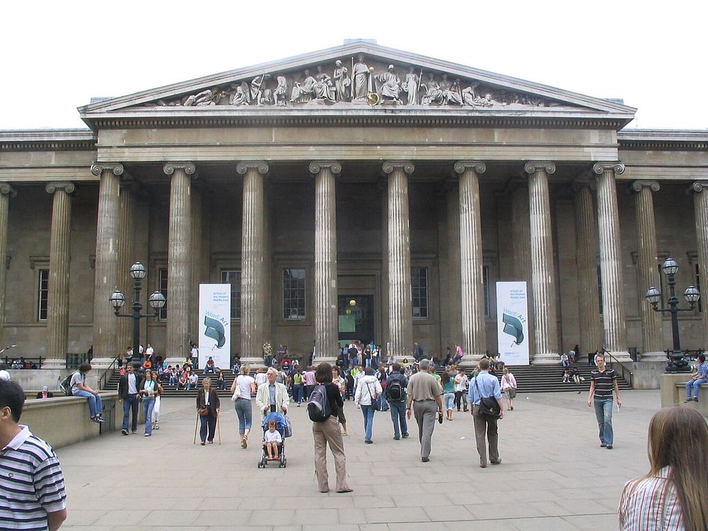 A crowded museum forecourt faces a wide Ionic colonnade topped by a sculpture-filled triangular pediment.