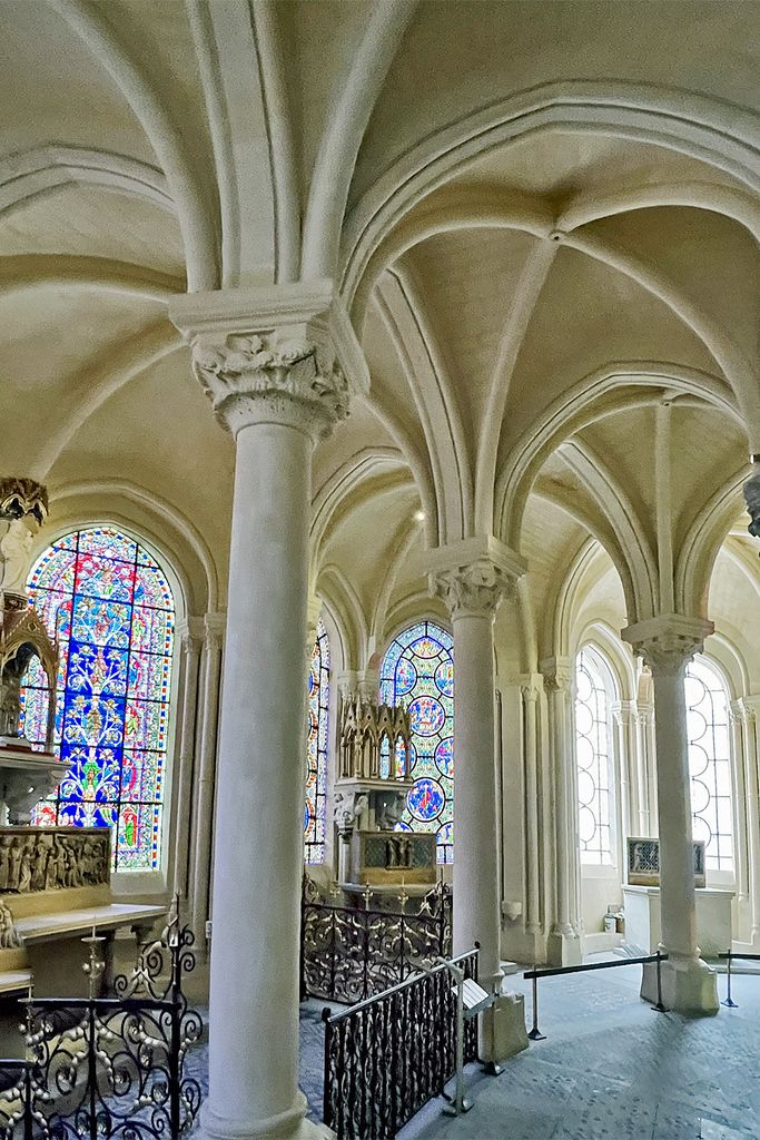 Slender columns support branching pale ribs above adjoining chapel bays filled with stained glass and enclosed by iron railings.