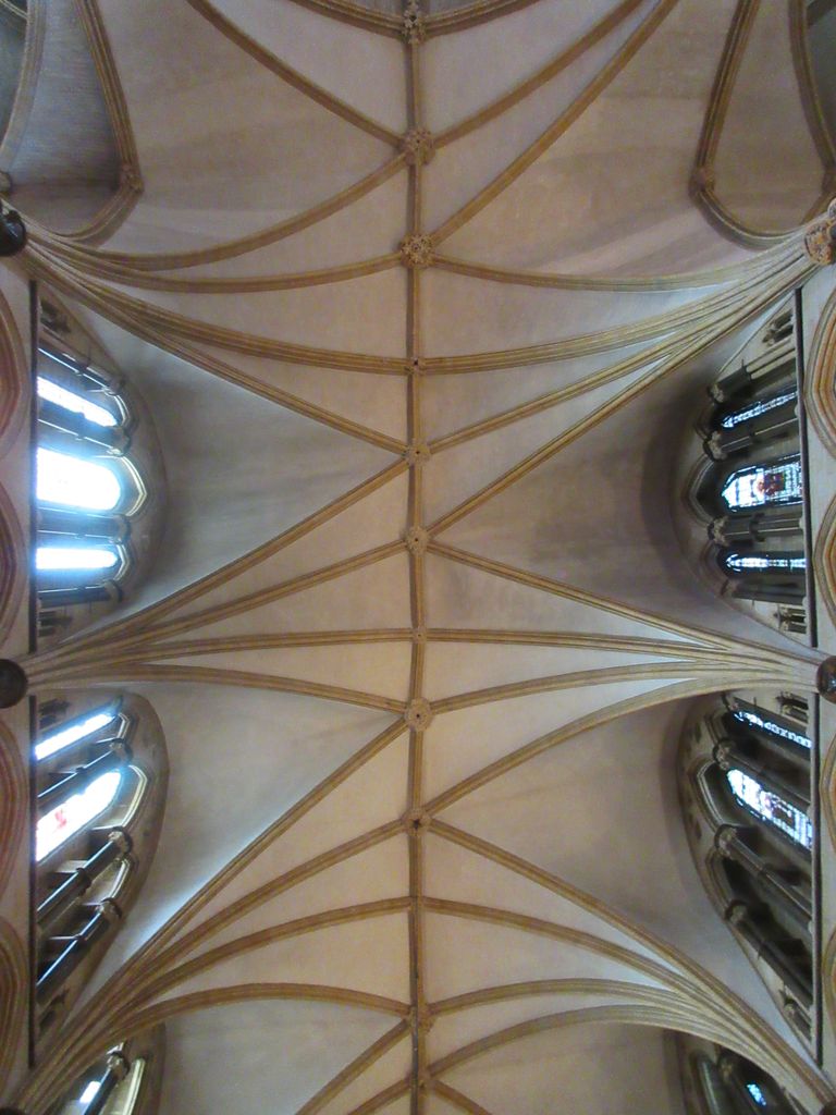Offset ribs and bosses cross a pale choir ceiling asymmetrically along a central ridge between high windows.