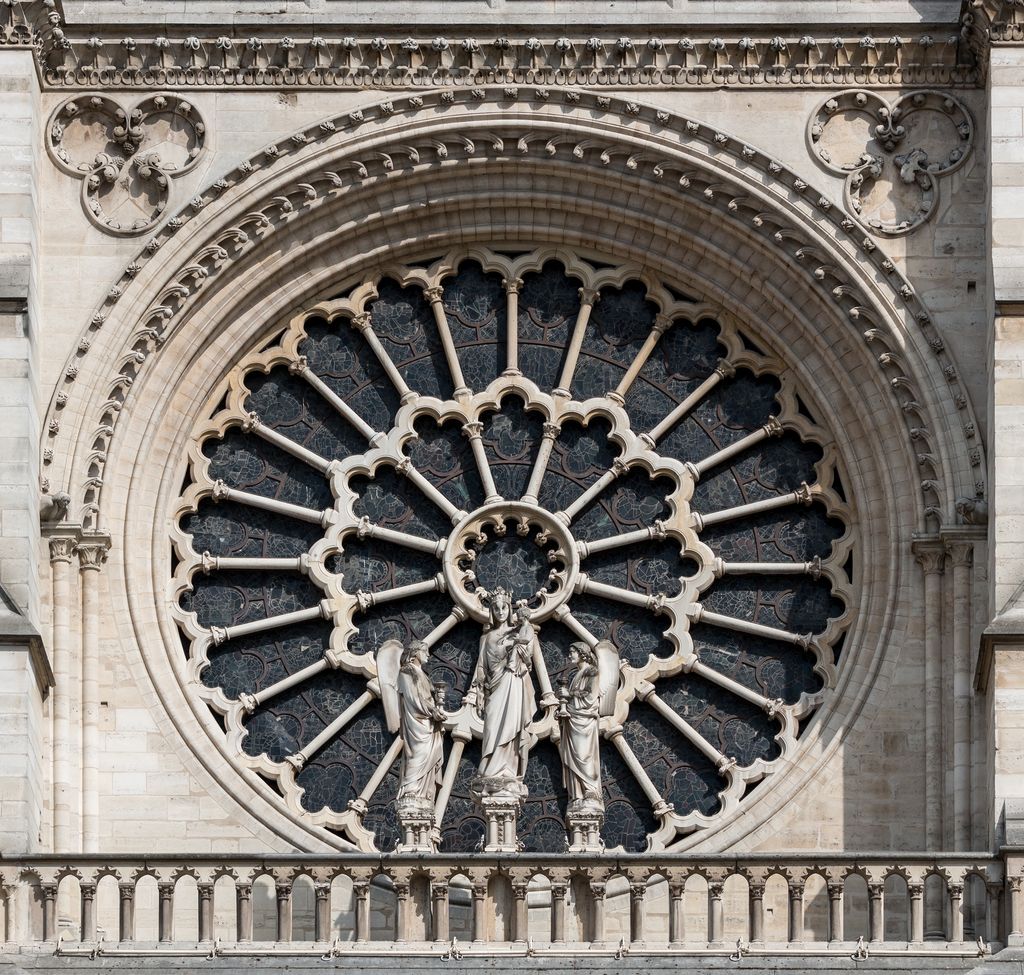 Pale radial stone bars and nested foils divide a large dark-glazed rose above portal sculpture and below carved façade mouldings.