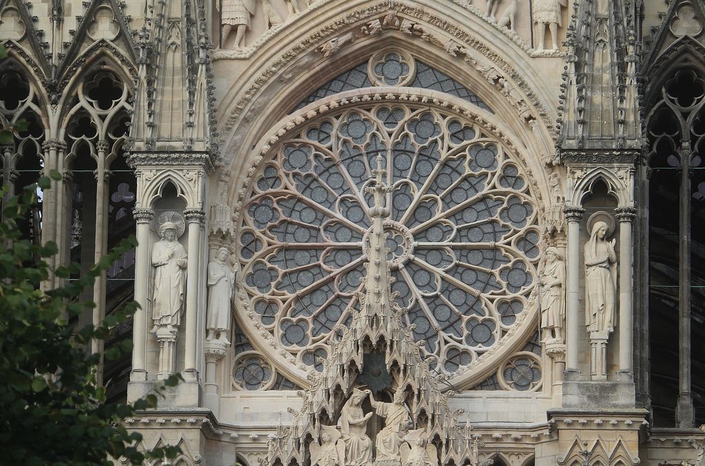 A large circular stone rose with radiating bars and small foils sits above a sculpted portal within a richly carved Gothic façade.