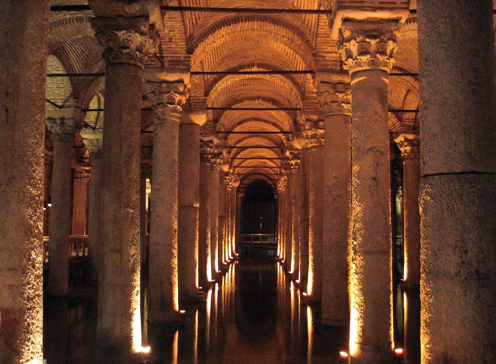 Rows of stone columns support repeating brick arches and vaults above a dark water surface.