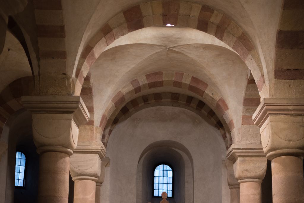 Smooth ceiling surfaces intersect above cushion capitals between red-and-pale banded arches; the diagonal intersections have no projecting stone ribs.