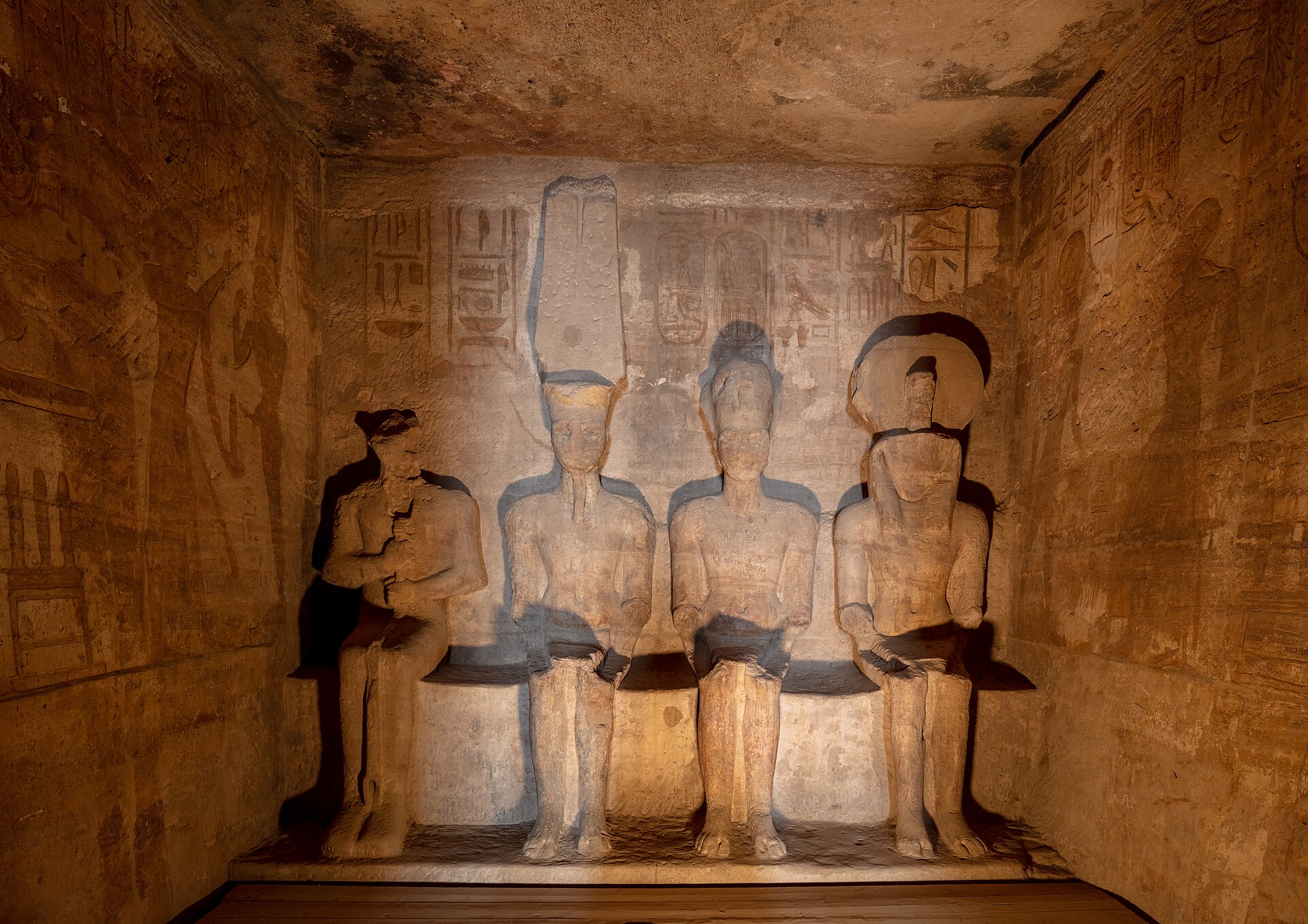 Great Temple sanctuary with four seated stone figures and hieroglyphic-carved side walls under modern interior lighting.