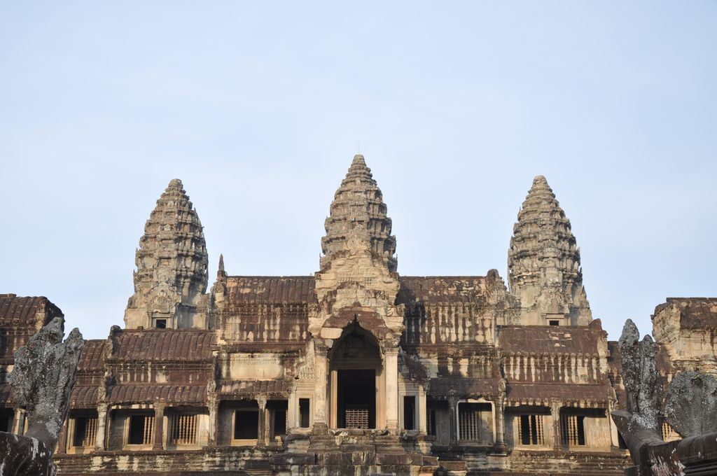 Three weathered sandstone towers with tiered lotus-bud profiles rise above dark galleries, steep steps and carved parapets.