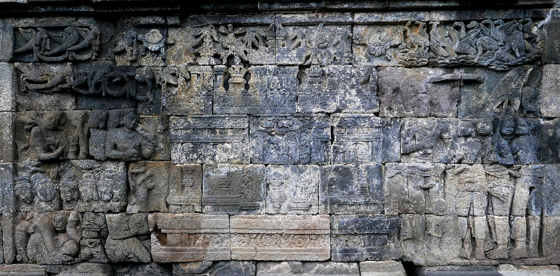 Borobudur carved wall showing small gabled building forms within a larger relief with birds and worn figures.