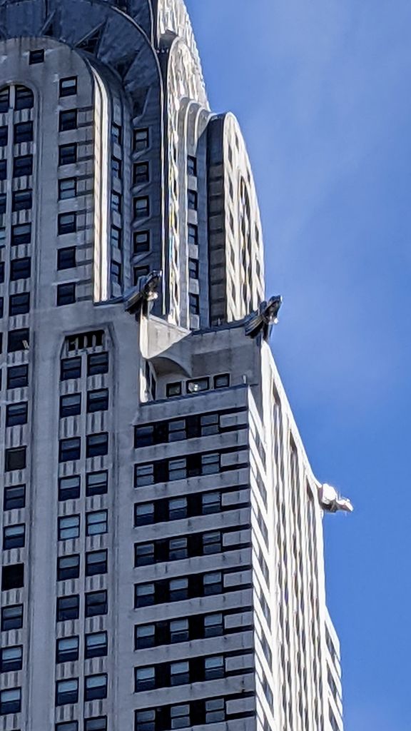 Three metal eagle-headed sculptures project from successive corners of a pale skyscraper beneath its silver crown.