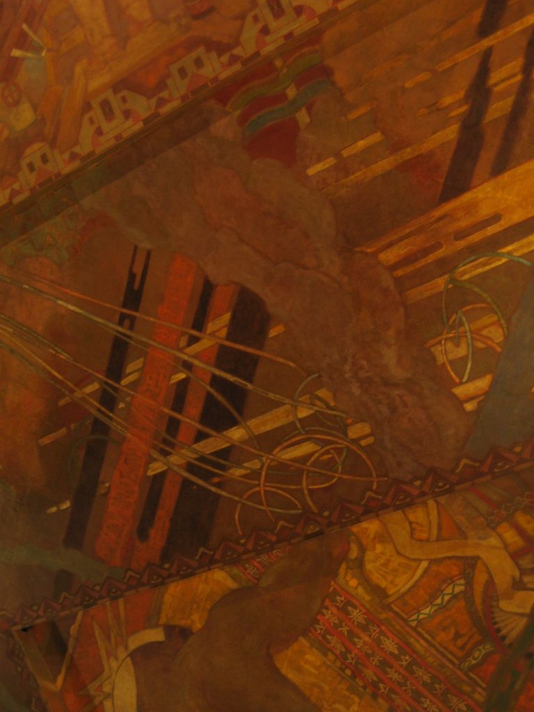 A dark warm-toned ceiling painting contains aeroplanes, beams, geometric patterns and industrial or architectural forms seen at a steep angle.