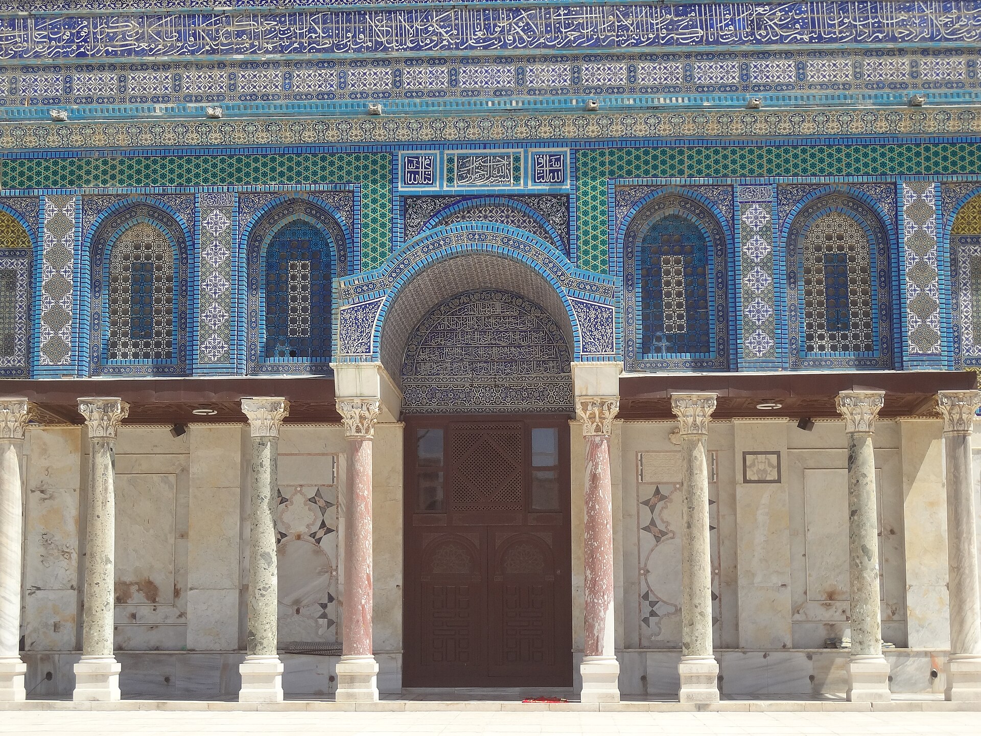 Southern Dome of the Rock entrance with a central doorway, marble columns and dense blue-tile and Arabic inscription bands.