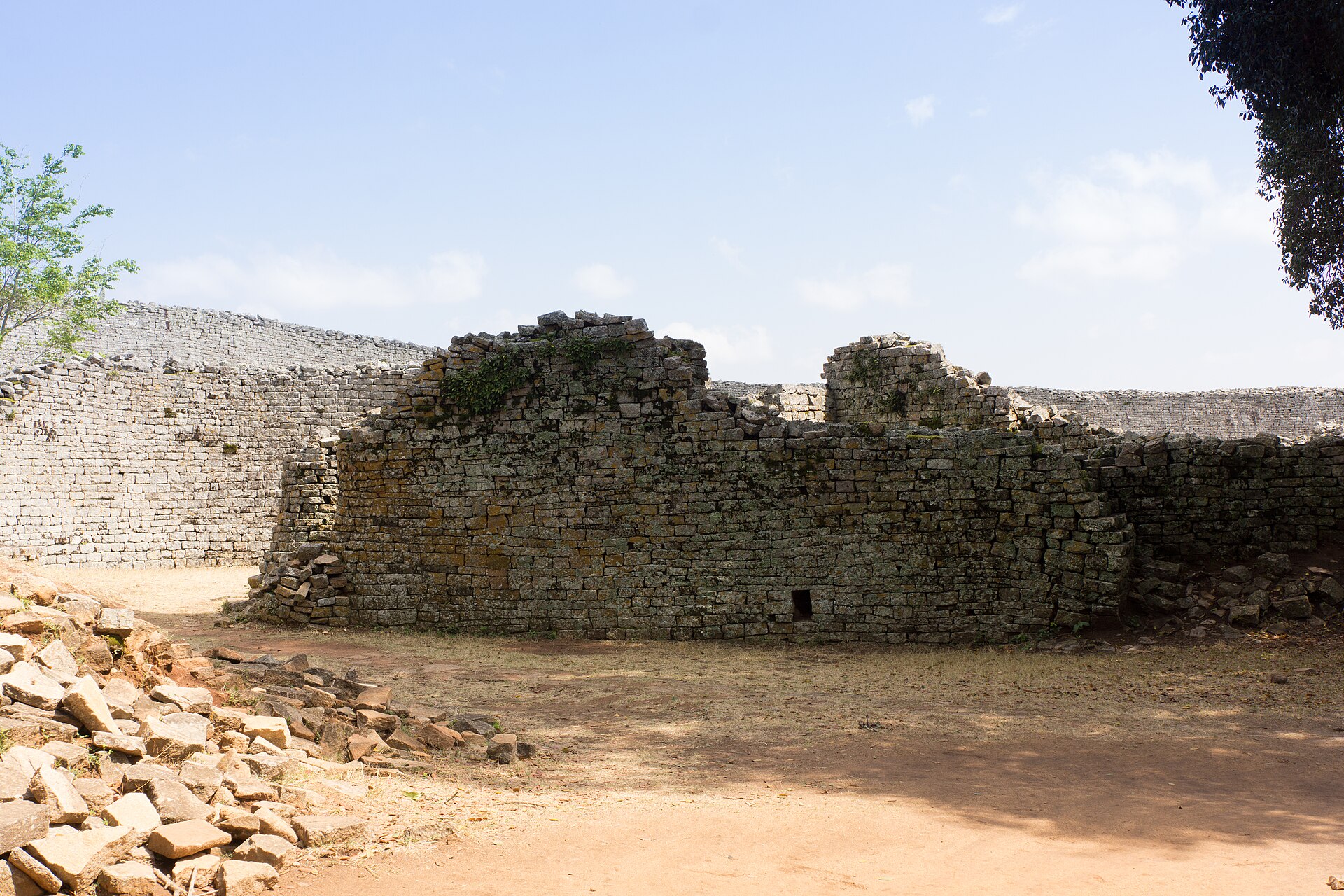 Several lower broken stone partitions with the tall curving outer wall of the Great Enclosure behind.