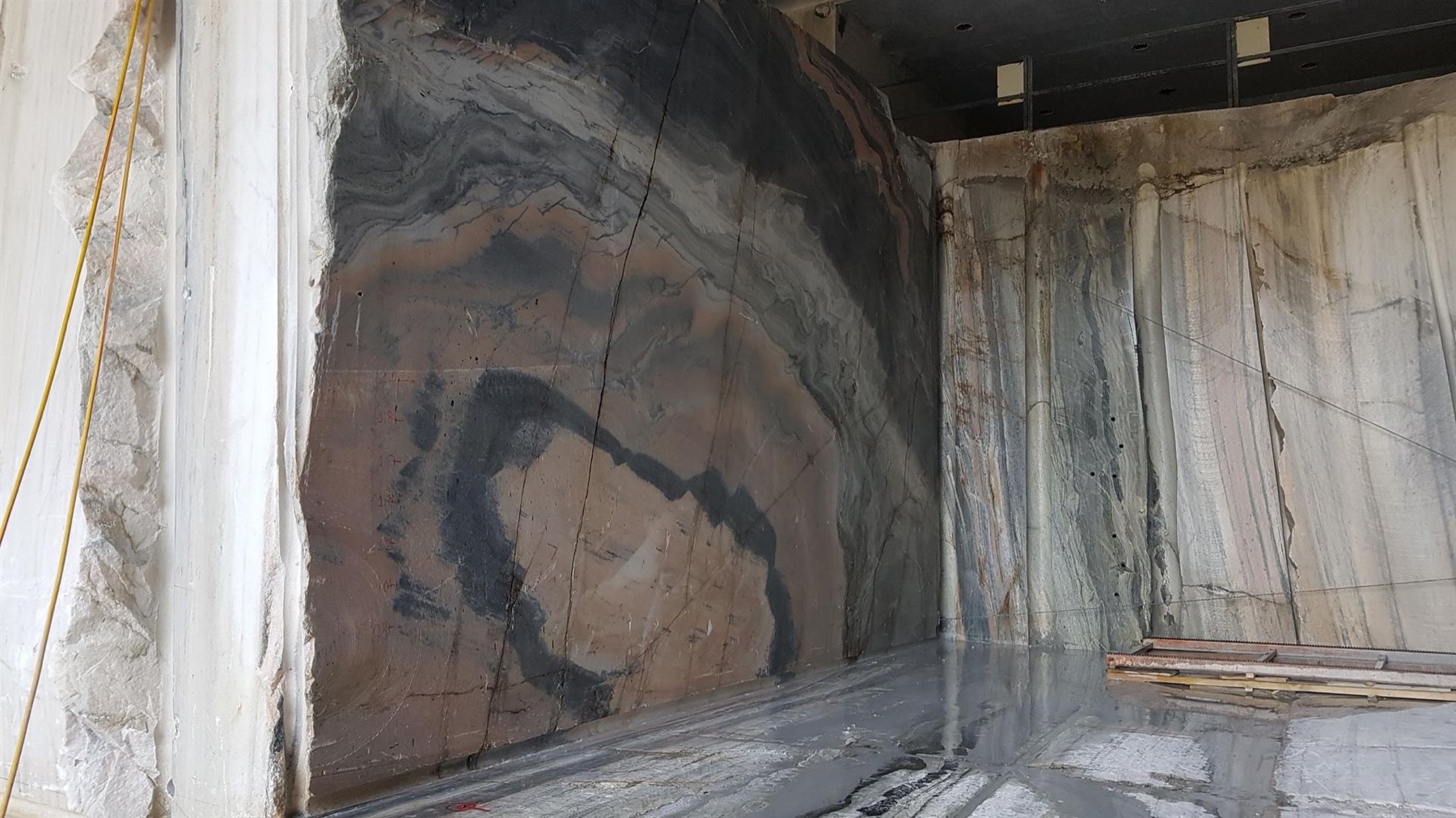 A cut chamber in the Candoglia quarry exposes grey, white and pink marble faces with saw marks and a wet working floor.