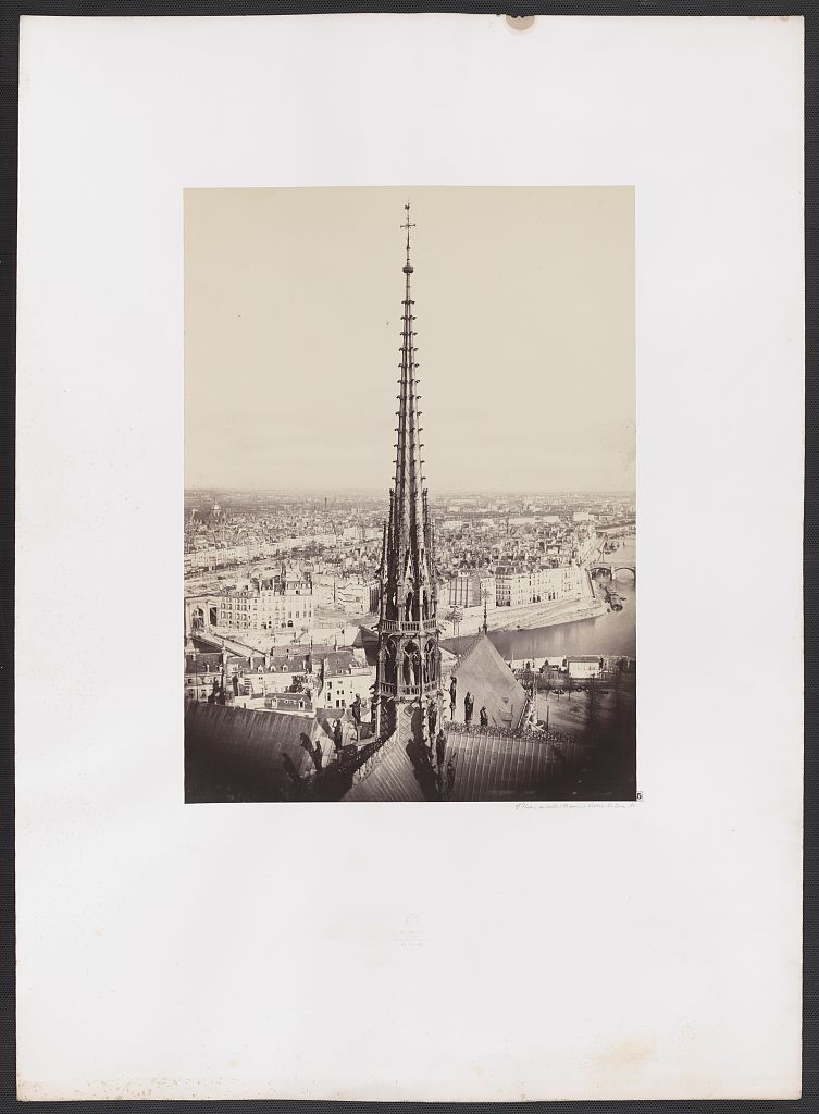 A small historic albumen photograph on a broad white mount shows Notre-Dame's tall nineteenth-century crossing spire, roof statues and the Paris cityscape beyond.