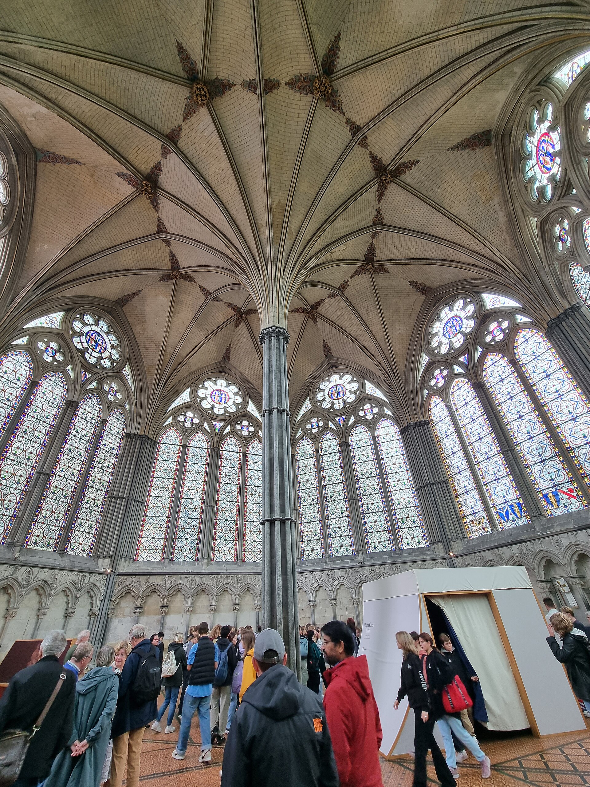 Salisbury chapter house interior with a slender central pier branching into radiating vault ribs above traceried windows and the sculpted wall arcade.