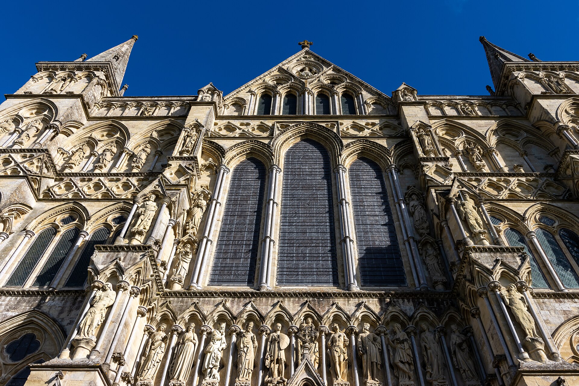 Upward daytime view of Salisbury Cathedral's west front showing lancets, arcaded niches, sculpted figures, gable and corner turrets.