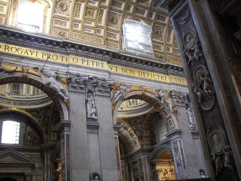 A colossal fluted pier divides two decorated arches beneath a gold-lettered inscription, sculpted figures and richly coffered vaults.