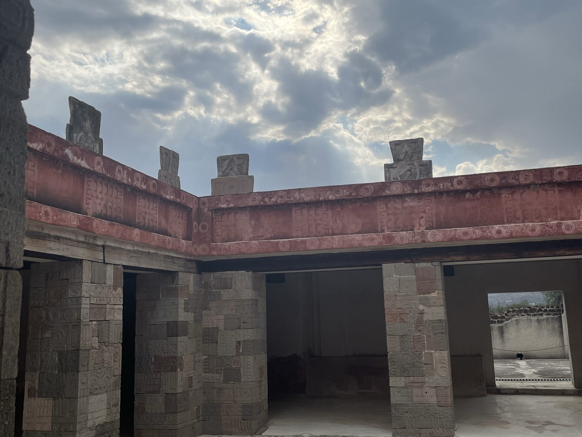 Corner of restored roofless courtyard with red framed bands, sculpted columns and merlon-like tops.