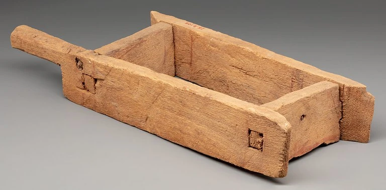 A wooden rectangular brick mould with joined boards and projecting ends.