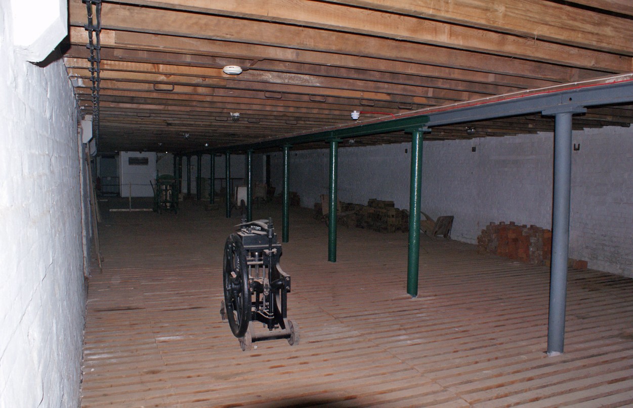 Machinery, posts and stacks of brick units beneath a timber ceiling in a former brickworks drying room.