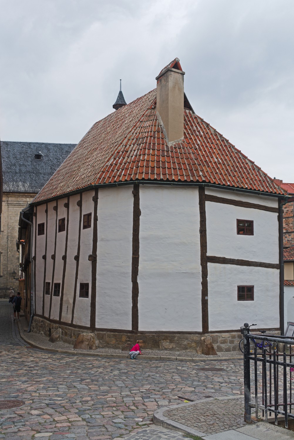 The Quedlinburg Ständerbau on a cobbled corner, with long dark posts, pale wall panels, small windows and a steep red-tiled roof.