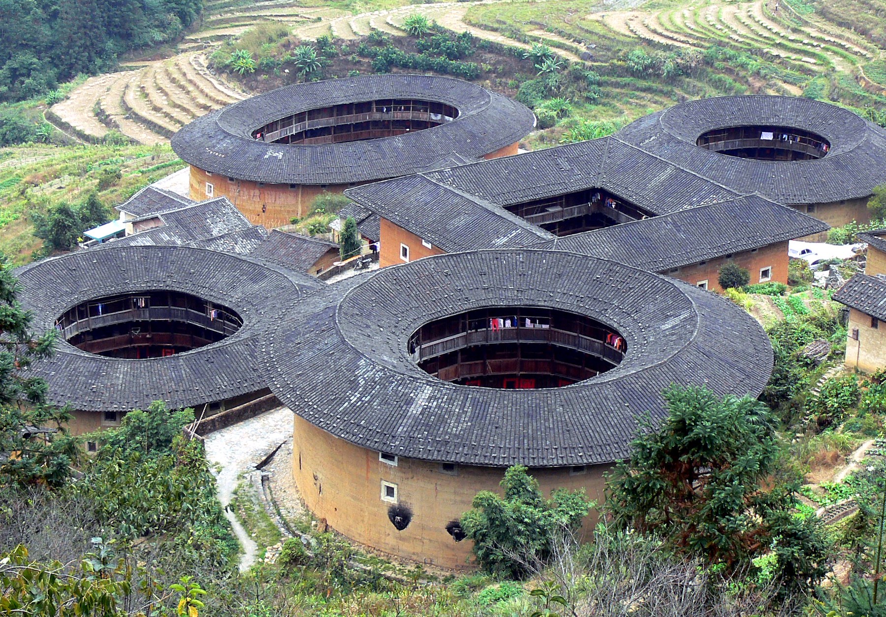 Elevated view of the circular and oval earthen tulou at Tianluokeng, with tiled roofs surrounding open courts.