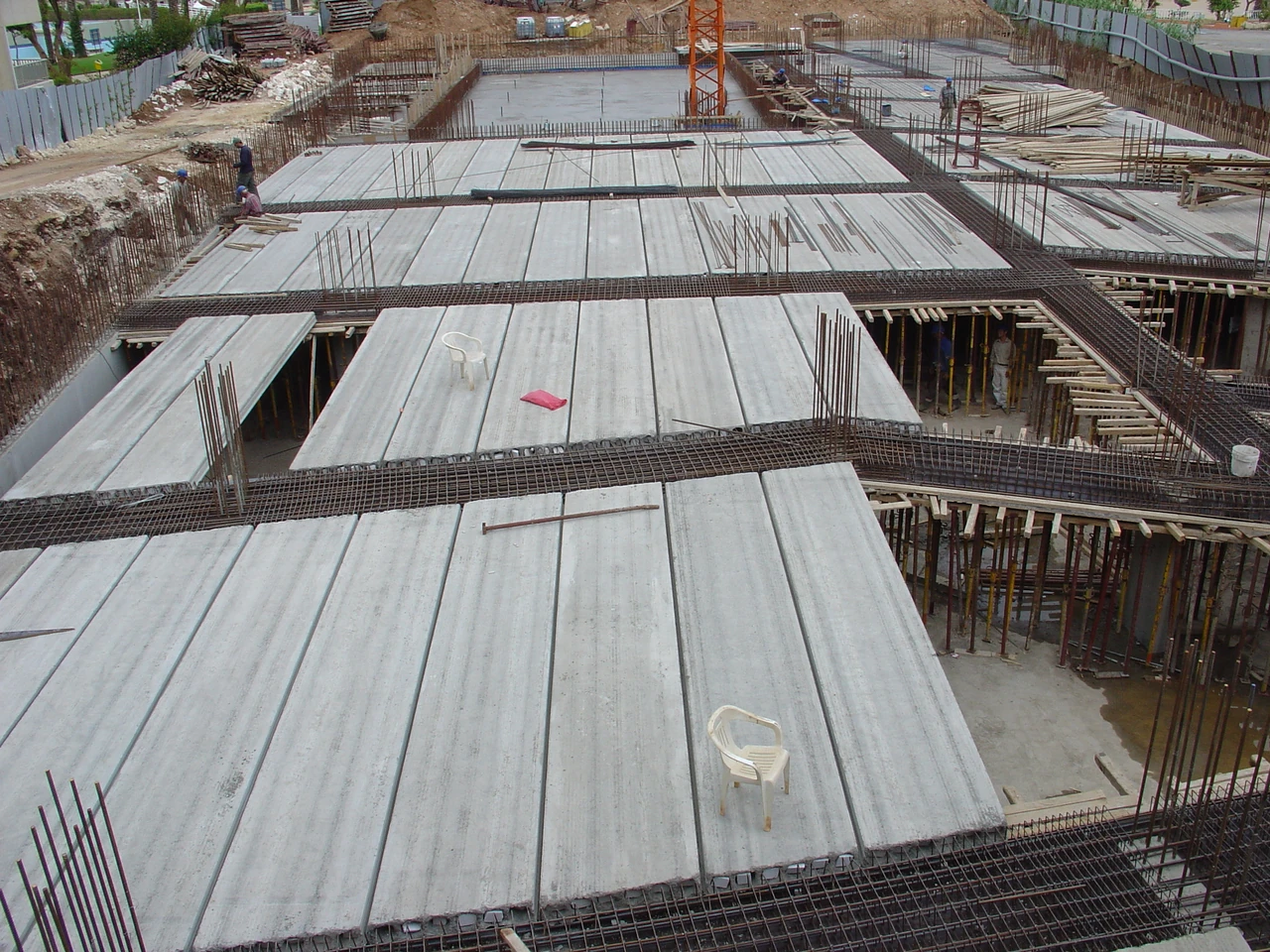 Precast floor units are laid between reinforced zones, with timber supports visible beneath gaps in the construction.