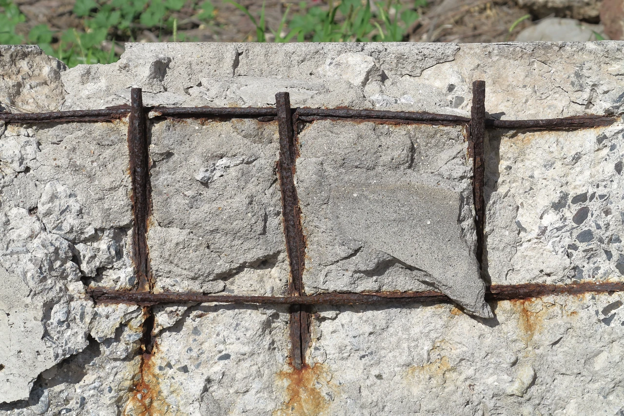 Rust-coloured reinforcement crosses a damaged concrete face where parts of the covering material have detached.