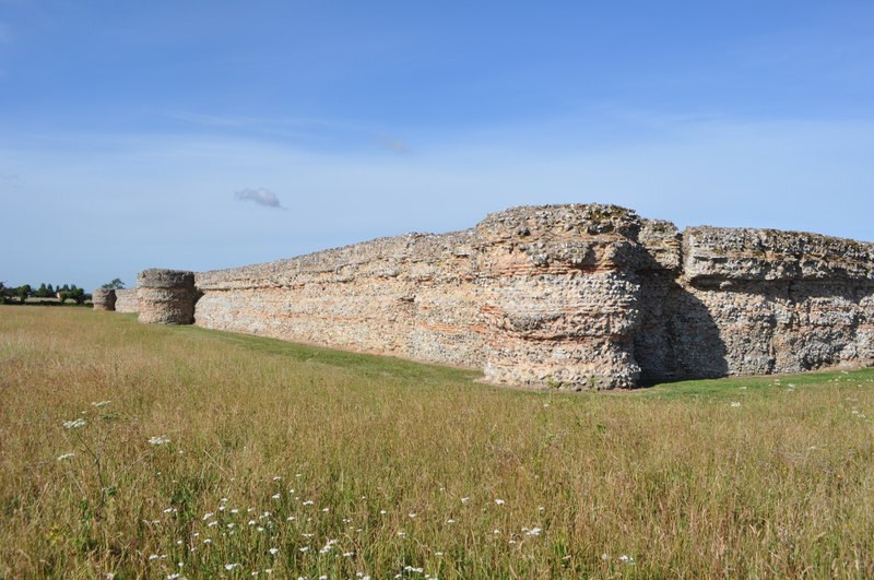 Long surviving Burgh Castle wall and rounded bastion with horizontal red tile bands and flint facing.